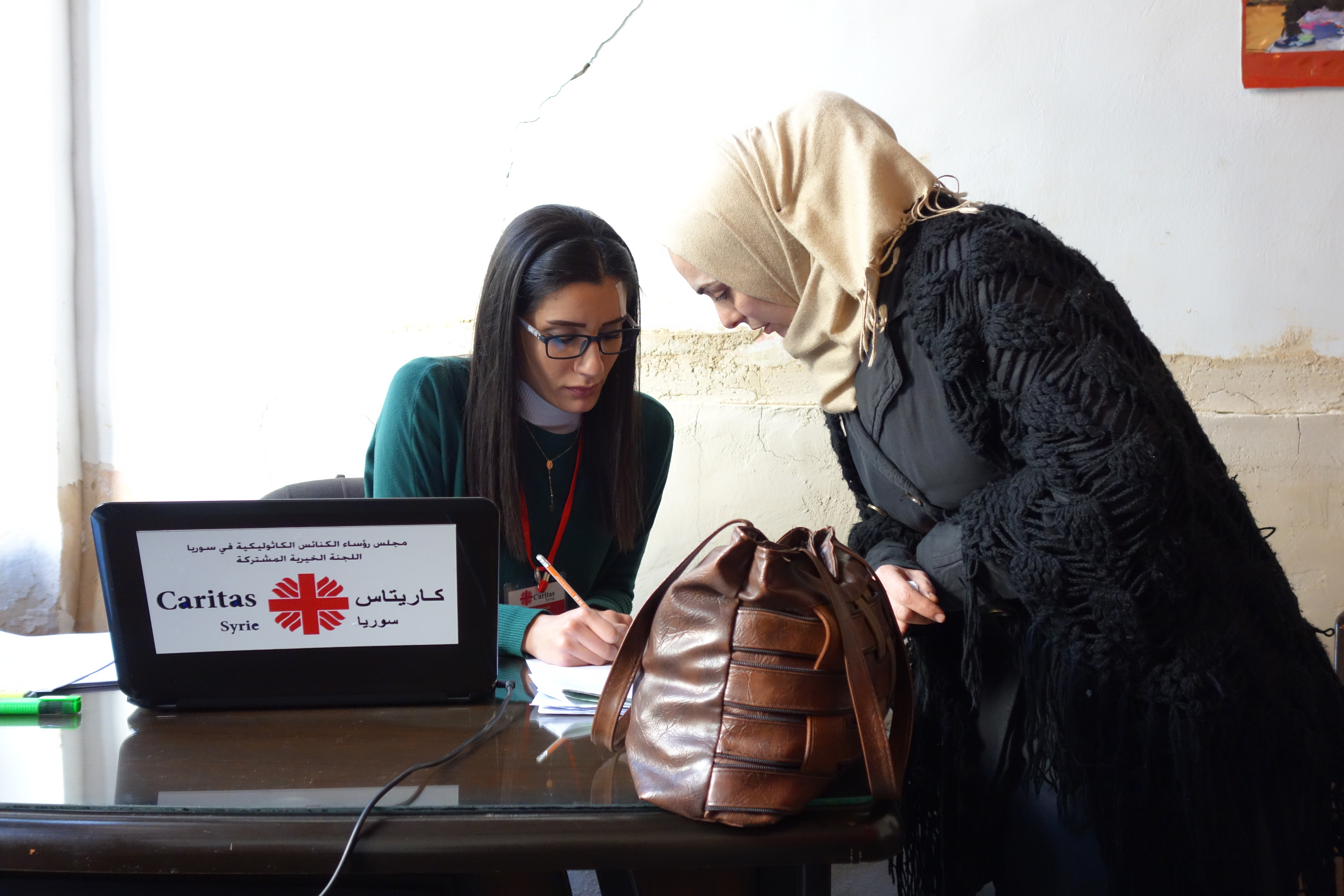 Eine Frau mit Kopftuch wird von einer Mitarbeiterin der Caritas Syrien als Bedürftige registriert
