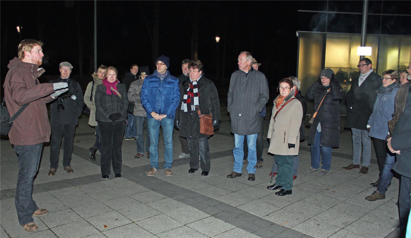 Gruppe steht auf dunklem Platz. Eine Person spricht.